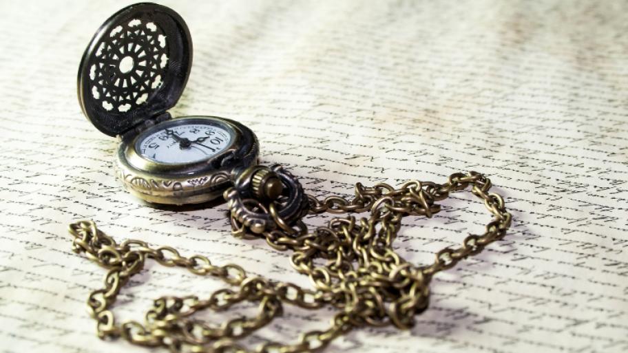kleine goldene Uhr mit langer Kette auf beschriebenem Papier
