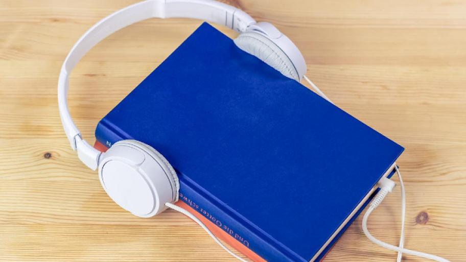 Ein blaues Buch liegt auf einem Laminatboden. Um das Buch sind weiße Kopfhörer.