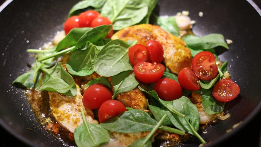 Gebratenes Hähnchen in einer Pfanne mit Tomaten und Basilikum.