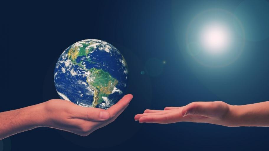 zwei geöffnete Hände gegenüber, auf der linken liegt eine Weltkugel, die rechte ist leer, streckt sich der linken entgegen, im Hintergrund blauer Himmerl und die Sonne oben rechts