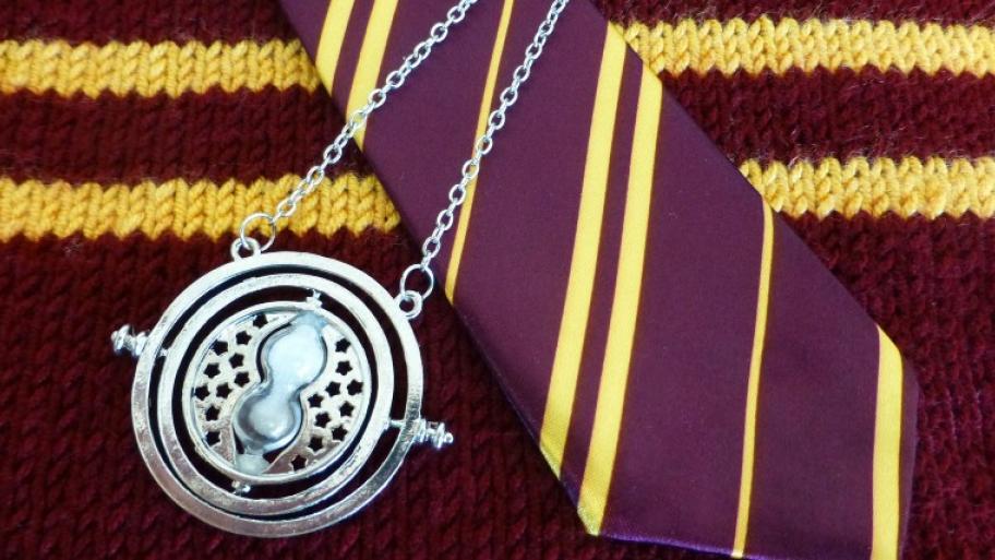 Symbole des Harry-Potter-Hauses Gryffindor: auf einem scharlachrot-gold-gestreiftem Schal liegt eine Gryffindor Krawatte und ein silberner Zeitumkehrer