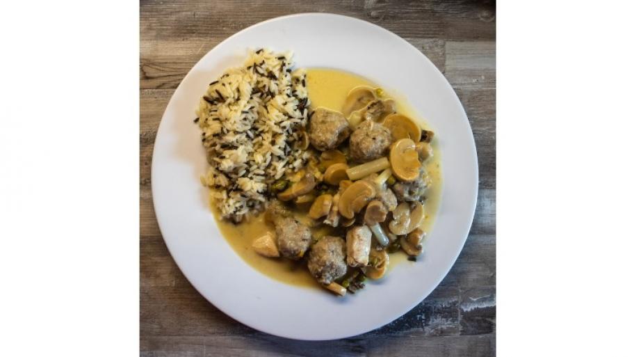ein weißer Porzellanteller, darauf eine Portion Wildreis, dazu Hühnerfrikassee bestehend aus Fleisch, Pilzen und Soße
