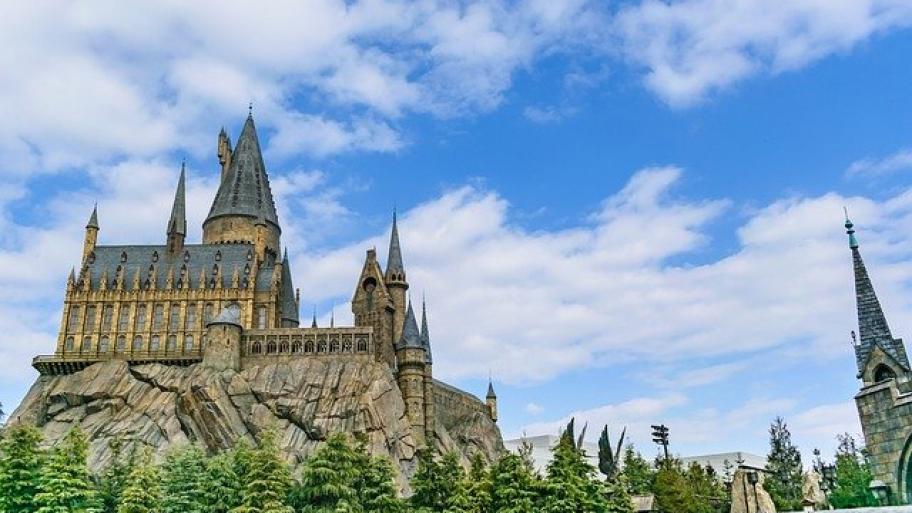 das Internat "Hogwarts" aus den Harry Potter Büchern, ein Schloss auf einem Felsen, davor grüne Bäume, im Hintergrund blauer Himmel und weiße Wolken