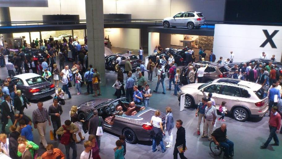 ein Ausstellungsraum auf der Internationalen Automobilausstellung: mehrere Fahrzeuge umringt von vielen Zuschauer*innen