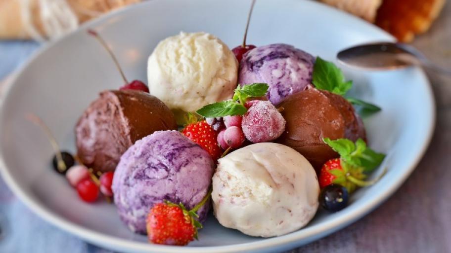auf einem weißen Porzellanteller verschiedene Eiskugelsorten, garniert mit Beerenfrüchten und frischer Minze