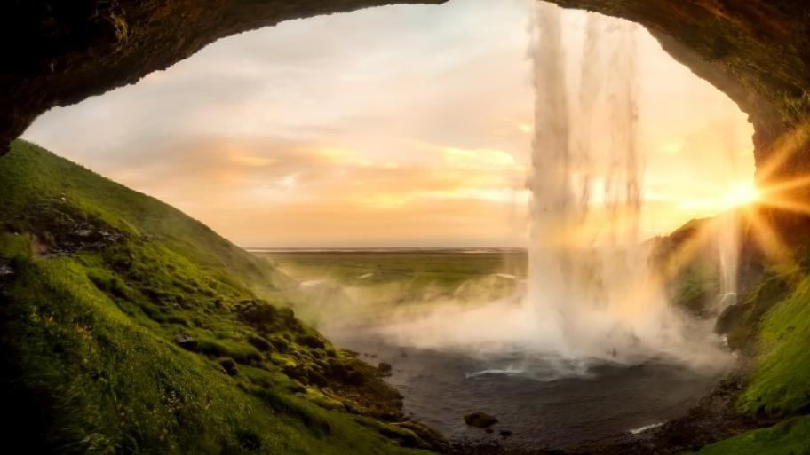 Blick aus einer Höhle, davor ein Wasserfall, auf grüne Ebenen