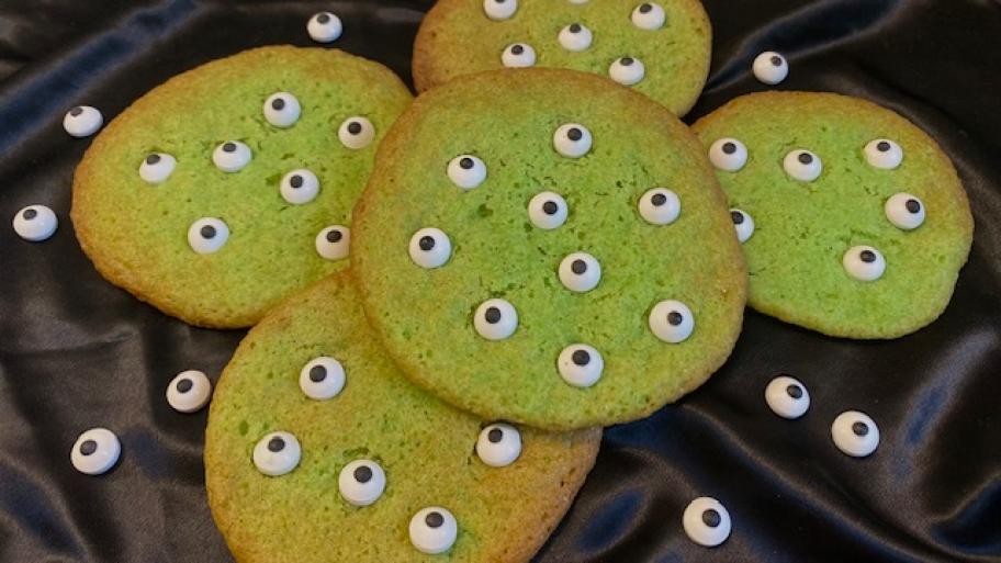 Zu sehen sind grüne Cookies, die mit sehr vielen Zuckeraugen verziert sind.
