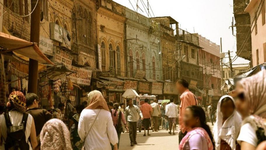 Viele Menschen mit luftiger, beiger Kleidung auf einer sandigen Straße in Indien.