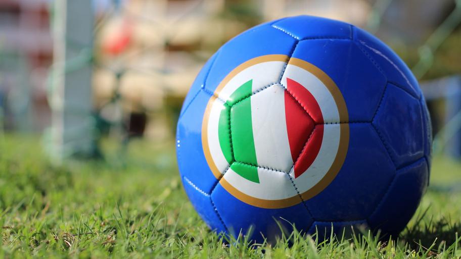 ein blauer Fußball mit einer runden Italien-Flagge liegt auf einem Fußballfeld