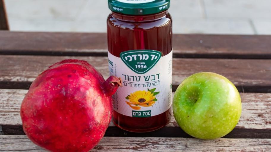 auf einem hölzernen liegt ein roter Granatapfel, daneben ein Glas Honig mit Hebräischer Aufschrift, daneben ein grüner Apfel