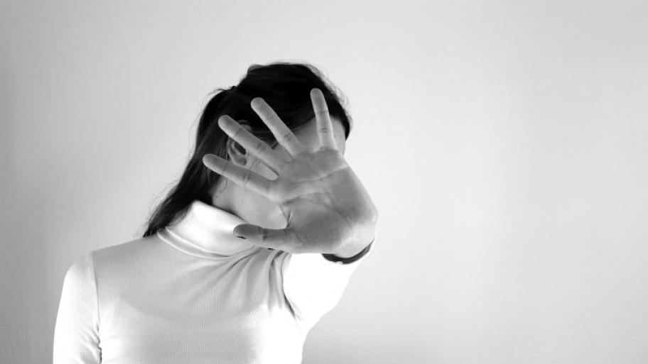 eine Person mit ausgestrecktem Arm, die Hand in abwehrender Haltung verdeckt das Gesicht, Foto in schwarz-weiß