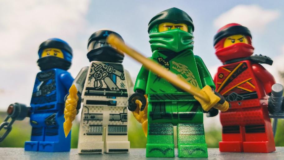 Vier Lego-Giguren stehen nebeneinander. Zuerst ein blauer Lego-Ninja. Daneben ein seilberfarbener, daneben ein grüner und ganz rechts ein roter.