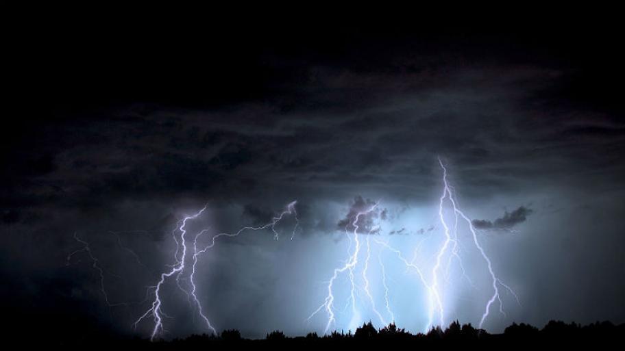 Zu sehen sind drei große Blitze, die über den dunklen Himmel zucken. 