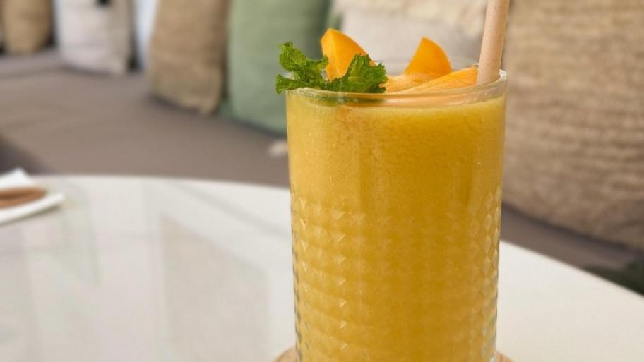 Gelber Mango Lassi im Glas, das in einem Wohnzimmer steht. 