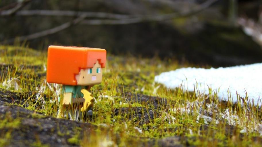 eine kleine Minecraft-Spielfigur steht auf grüner Wiese, im Hintergrund ein Rest Schnee