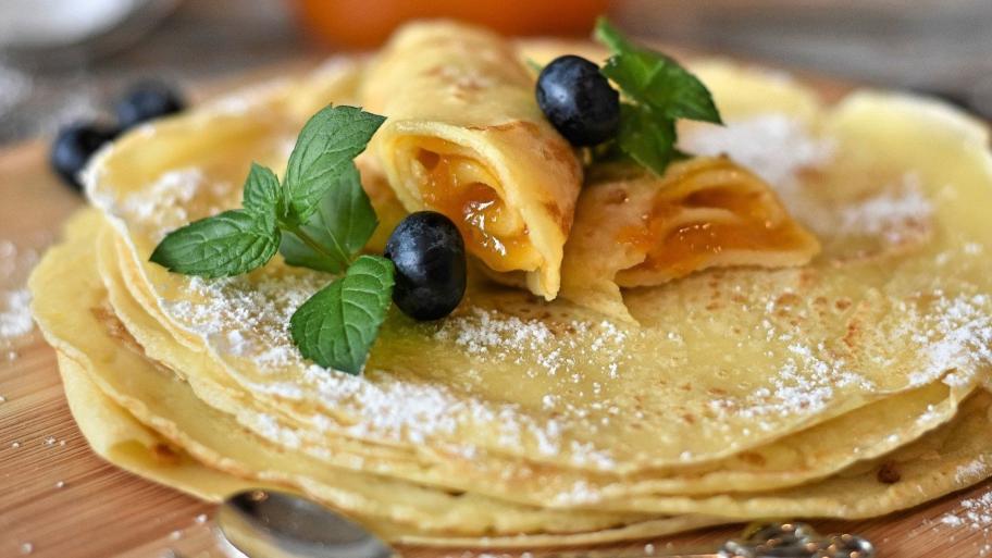 auf einer Holzunterlage ein Stapel Crepes, dekoriert mit Puderzucker, frischer Minze und dunklen Weintrauben
