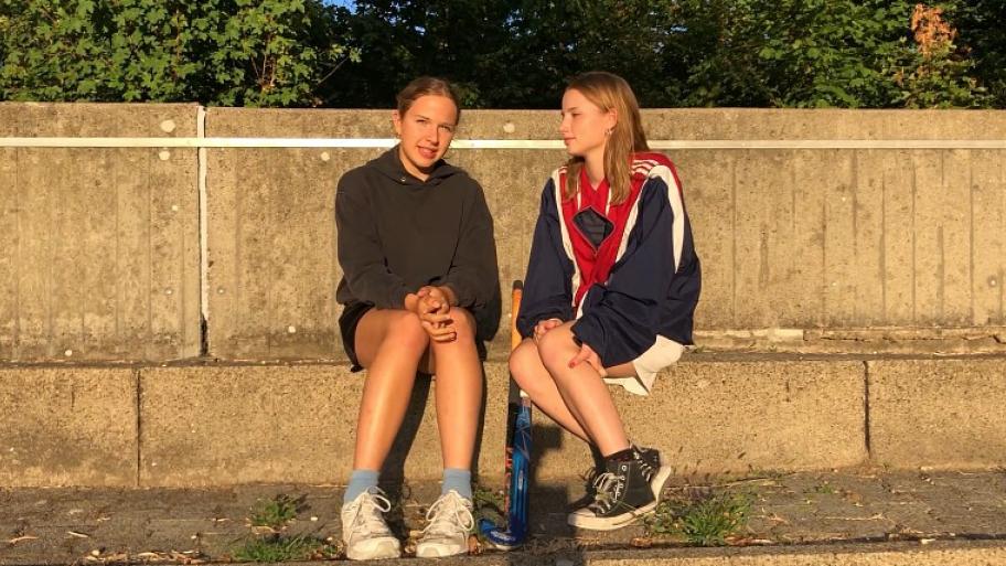 die beide Jugendtrainerinnen Pia und Clara sitzen in Sportbekleidung auf einer steinernen Tribüne
