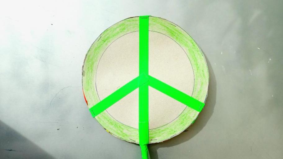 das Peacezeichen: ein runder Kreis aus Pappe, die Umrandung des Kreises und die Linien in knallgrün, Hintergrund grau