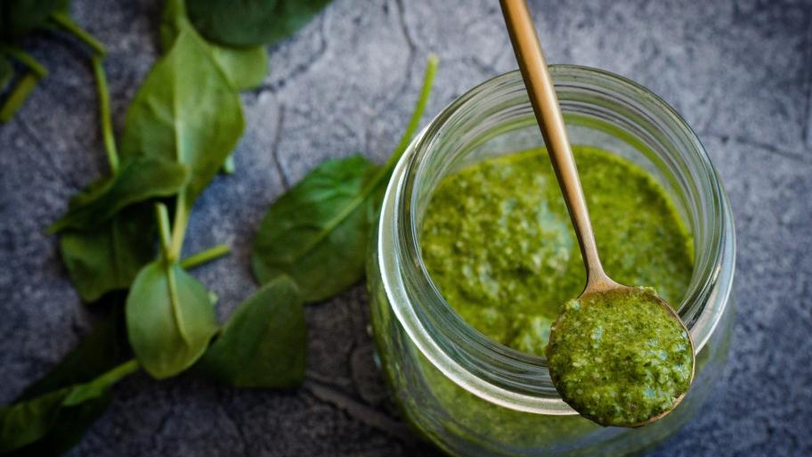 Ein Glas mit Pesto und ein Holzlöffel. 