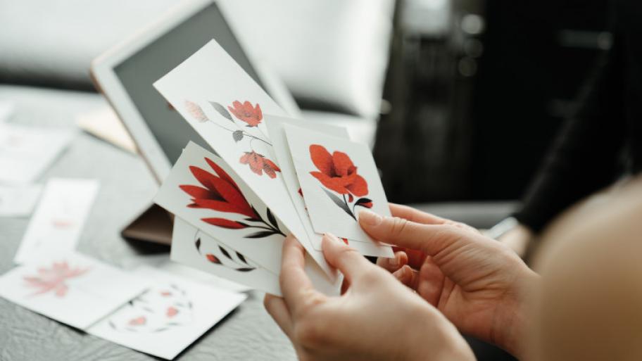 Eine Person hält weiße sticker mit roten Blumen darauf in den Händen