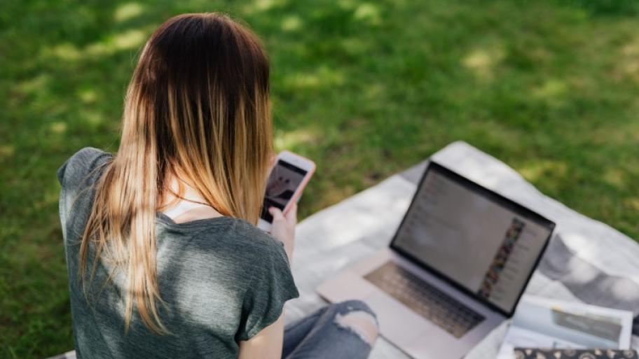 Teen am Handy und Laptop auf Picknickdecke