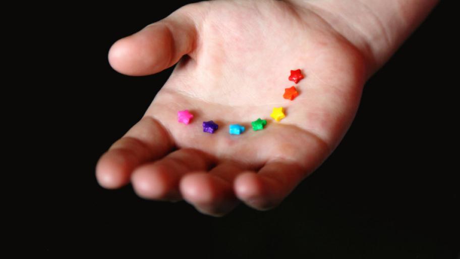 offene, flache Hand in der bunte Sterne liegen; sie bilden die Farben des Regenbogens