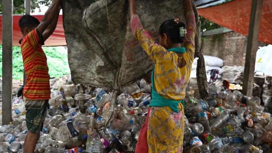 Zwei Kinder schütten Plastikflaschen aus einem Beutel auf beiner Müllhalde
