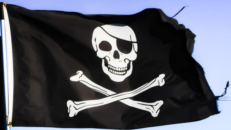 schwarze Piratenflagge flattert im Wind, darauf in weiß ein Totenschädel mit schwarzer Augenklappe, darunter zwei diagonal gekreuzte Knochen