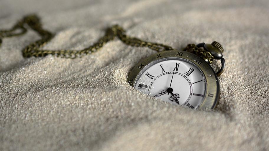 Eine Taschenuhr liegt im Sand. 