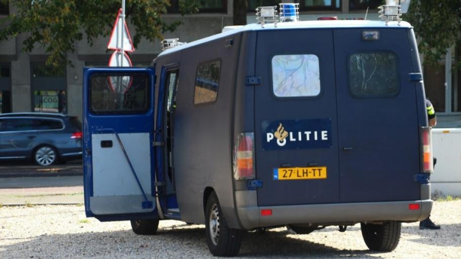 ein blauer Kastenwagen der niederländischen Polizei, zu sehen von hinten, steht geparkt auf einer Kiesfläche mit geöffneter Fahrertür