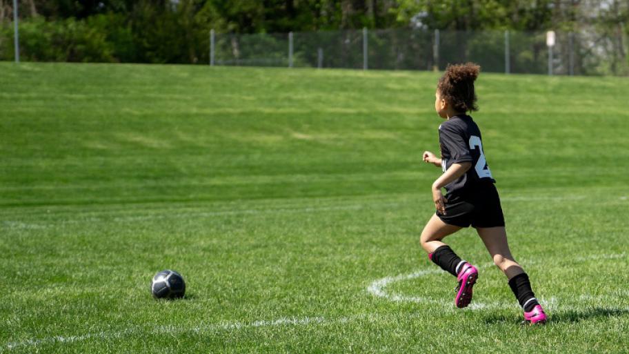 Mädchen in Fußball-Trikot rennt über ein Fußballfeld einem Fußball hinterher; sie hat die Nummer 2