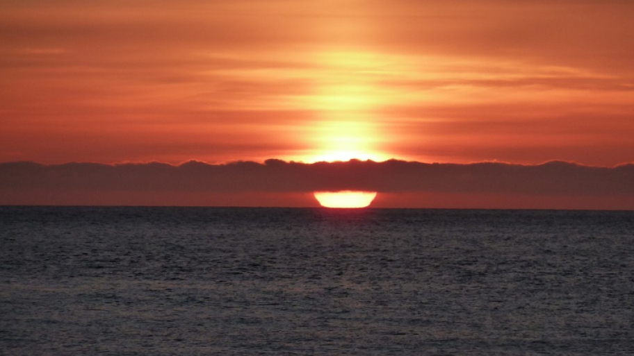 Sonnenuntergang hinter Wolkendecke über Wasser