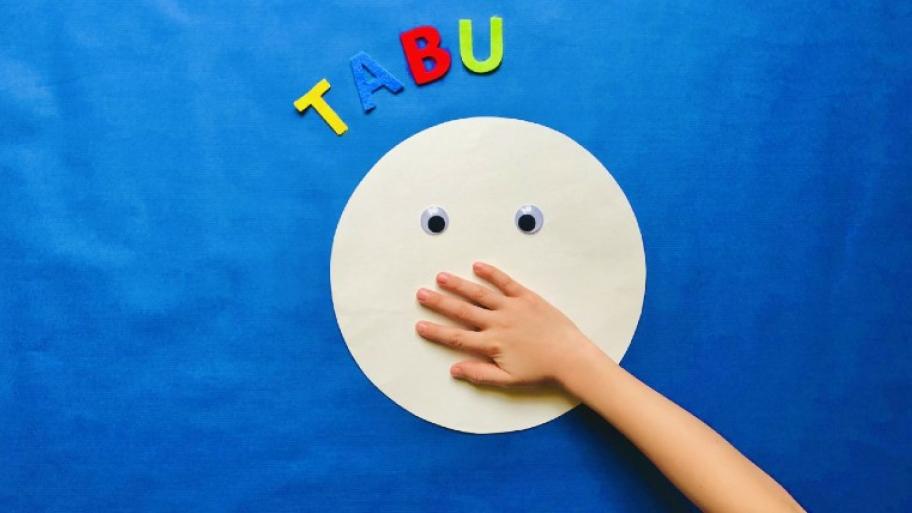 ein heller, großer, runder Smiley liegt auf blauem Untergrund, die Augen geöffnet, eine Kinderhand hält ihm den Mund zu, darüber in bunten Buchstaben das Wort "Tabu"