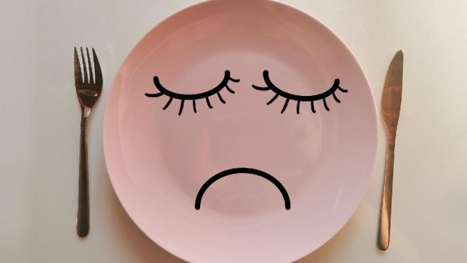 ein leerer Teller, Messer und Gabel daneben, auf dem Teller ist ein trauriges Gesicht gezeichnet