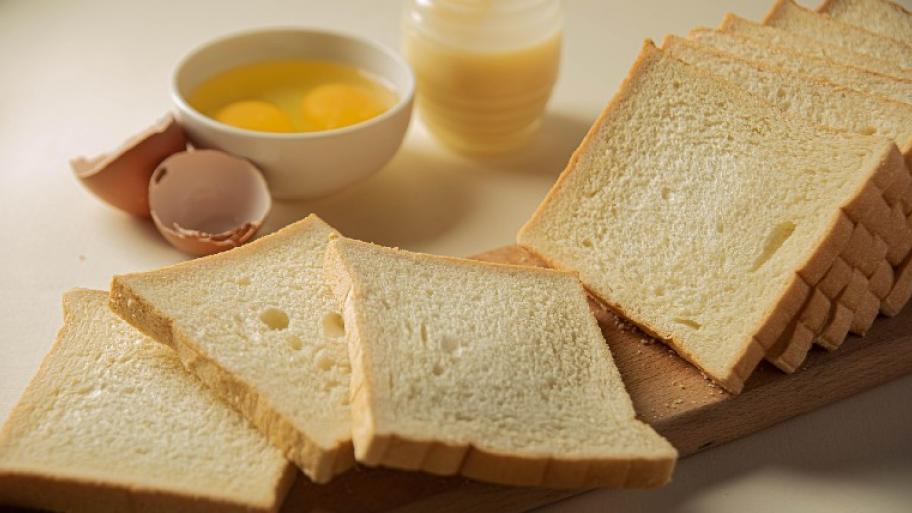 vier Toastbrotscheiben liegen auf einem Brett, dahinter steht eine Schüssel mit aufgeschlagenen Eiern