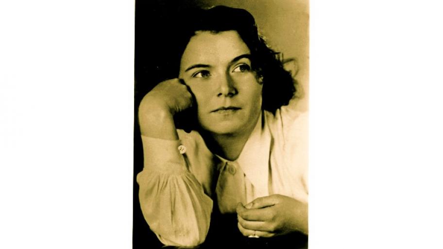 ein schwarz-weiß Porträt der Widerstandskämpferin Traute Lafrenz als junge Frau, sie trägt eine weiße Bluse, eine Ring an der linken Hand und stützt den Kopf auf die rechte Hand
