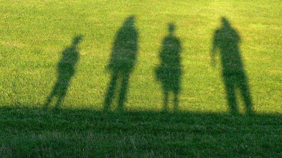 auf einer grünen Wiese die 4 Schatten einer Familie, Eltern und zwei Kinder