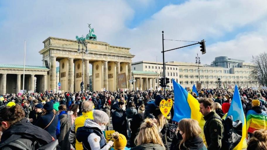 Eine große Masse steht vor dem Brandenburger Tor. Viele halten Demoschilder oder ukrainische Flaggen (gelb-blau) in den Händen.