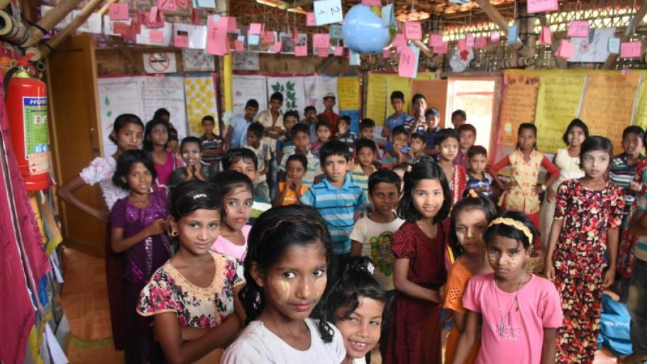 eine Schulklasse von circa 40 Kindern im Flüchtlingscamp Kutupalong in Bangladesch, die Kinder stehen in mehreren Reihen aufgereiht, der Klassenraum ist bunt geschmückt