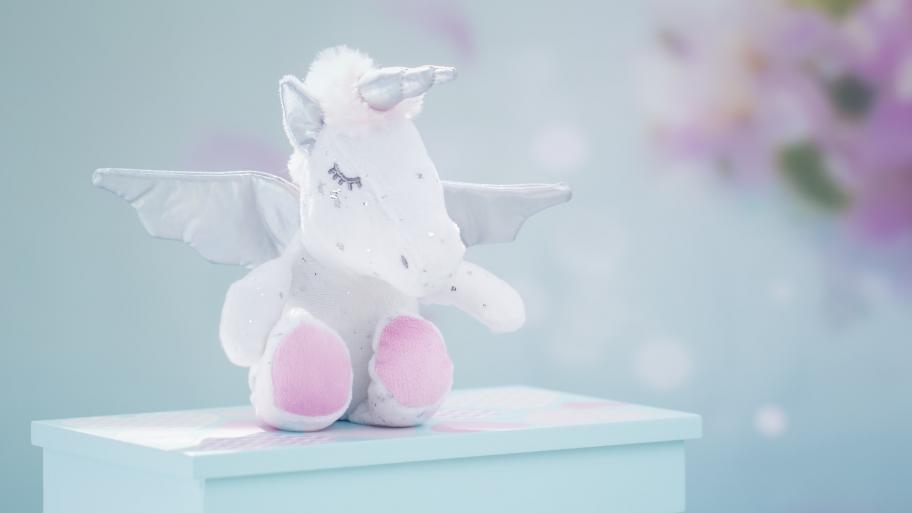 Ein weißes Einhorn als Kuscheltier sitzt auf einem Hocker