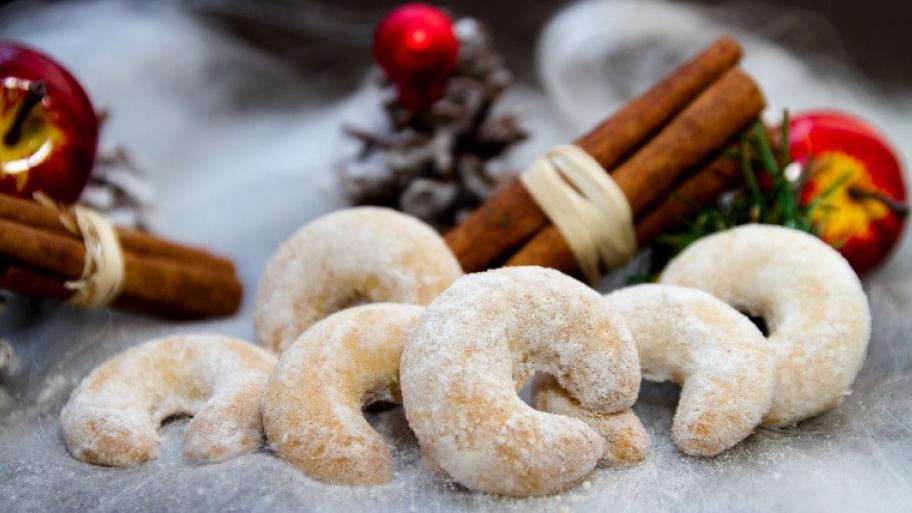 Vanillekipferl im Vordergrund, darunter Schnee und dahinter verschiedene weihnachtliche Dekoration wie Äpfelund Zimtstangen