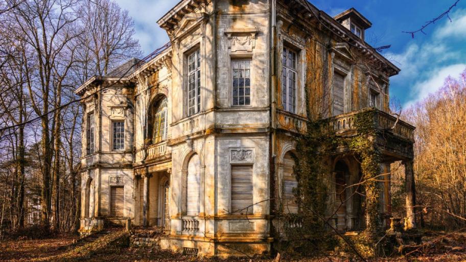 eine alte, verlassene Villa, die Fassade in Teilen von Efeu umrankt, im Hintergrund blauer Himmel