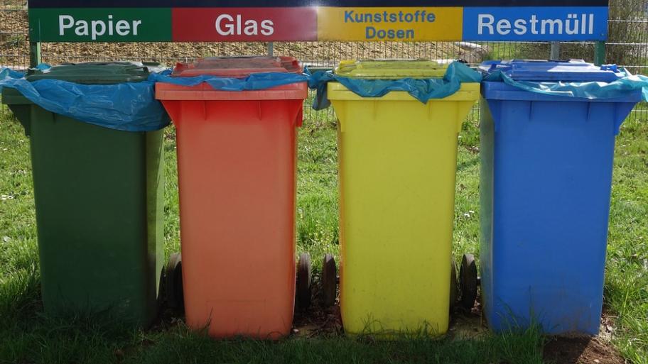 4 verschiedene Mülltonnen nebeneinander, von links nach rechts: grün für Papier, orange für Glas, gelb für Kunststoff und Dosen, blau für Restmüll 