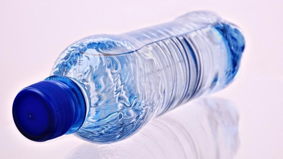 auf weißem Untergrund liegt eine volle, transparente Wasserflasche aus Plastik ohne Etikett mit dem blauen Deckel nach vorn