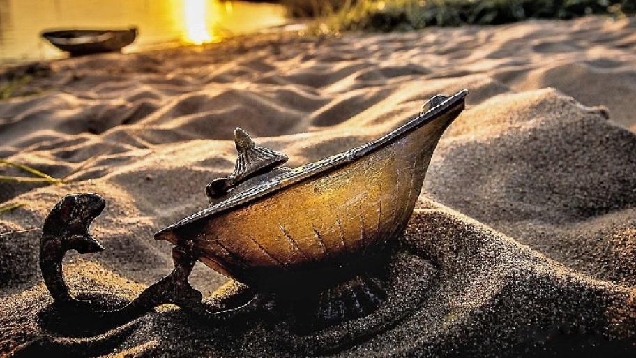 Zu sehen ist eine Wunderlampe, die am Strand im Sand liegt.