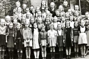 Eine Mädchenschulklasse bestehend aus ca. 42 Schülerinnen und ihrer Lehrerin stehen vor den Stufen ihres Schulgebäudes