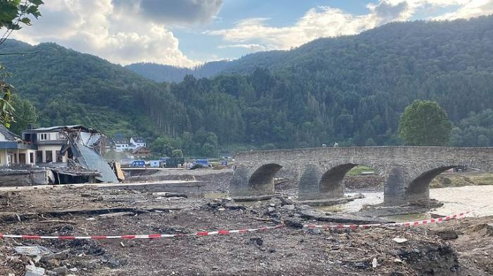 die zerstörte Brücke in Rech nach der Flutkatastrophe 2021, eingestürzte Häuser links, im Hintergrund bewaldete Berge und Wolken, im Vordergrund eine Schutthalde 