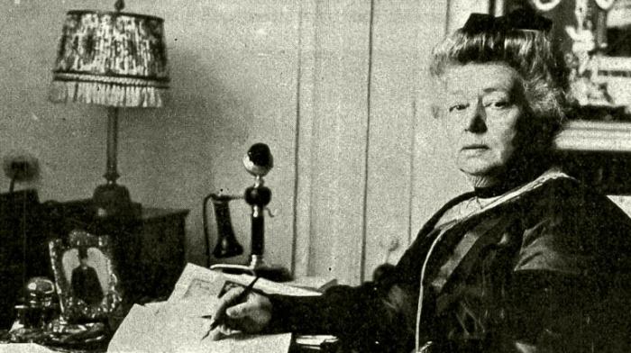 Schwarz-weiß-Fotografie der Friedensnobelpreisträgerin Bertha von Suttner in späteren Jahren zuhause an ihrem Schreibtisch mit Stift in der Hand