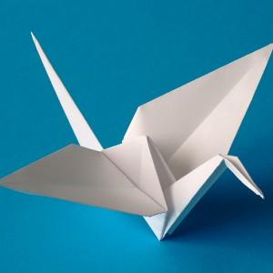 weißer aus Papier gefalteter Origami Kranich auf blauem Untergrund