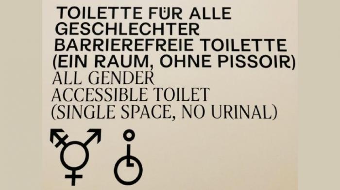 Schild an einer Toilettentür in schwarzer Schrift auf hellem Grund: Toilette für alle Geschlechter, barrierefreie Toilette (ein Raum, ohne Pissoir)